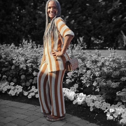 A beautiful woman with dark skin and long braided hair wearing a gold and white striped top and pants.